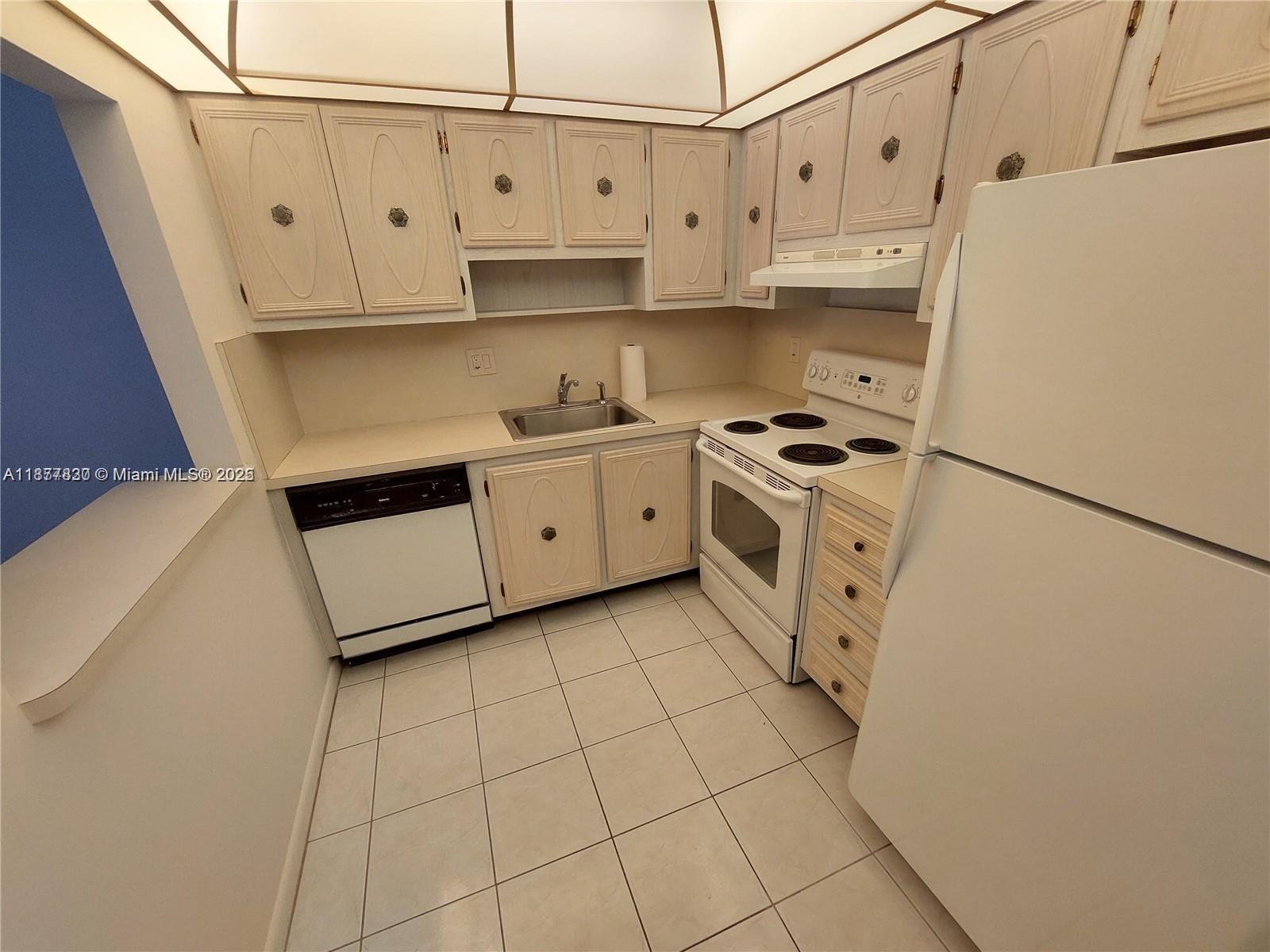 A small kitchen features white appliances, light-colored wooden cabinets, and a tiled floor — 257 S Cypress Rd # 438, Pompano Beach FL 33060, POMPANO BEACH, FL
