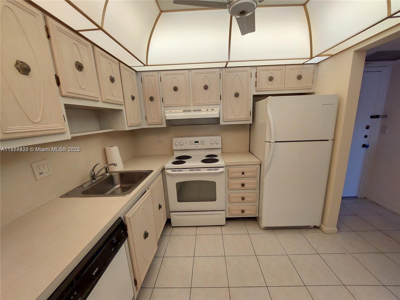 A kitchen features white appliances, light-colored cabinets, tiled flooring, and a recessed ceiling light — 257 S Cypress Rd # 438, Pompano Beach FL 33060, POMPANO BEACH, FL