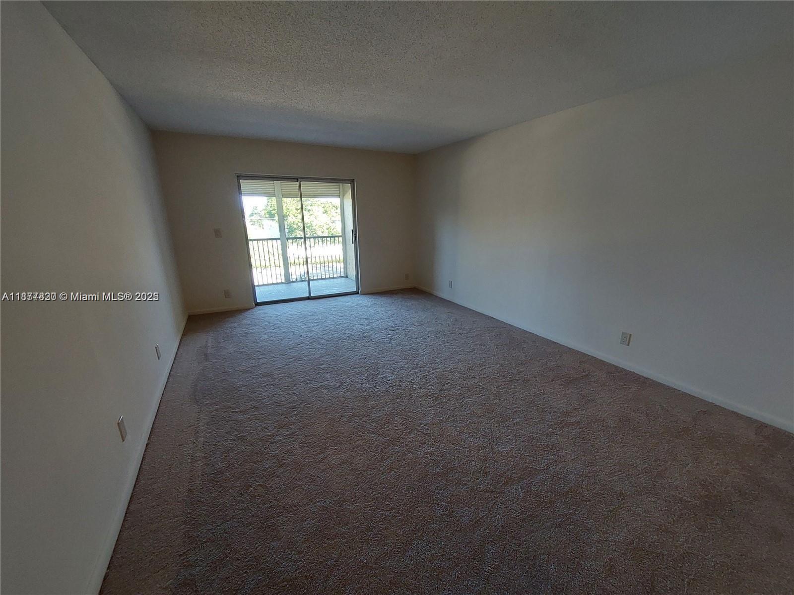 An empty room features beige carpeting, white walls, and a sliding glass door to a balcony — 257 S Cypress Rd # 438, Pompano Beach FL 33060, POMPANO BEACH, FL