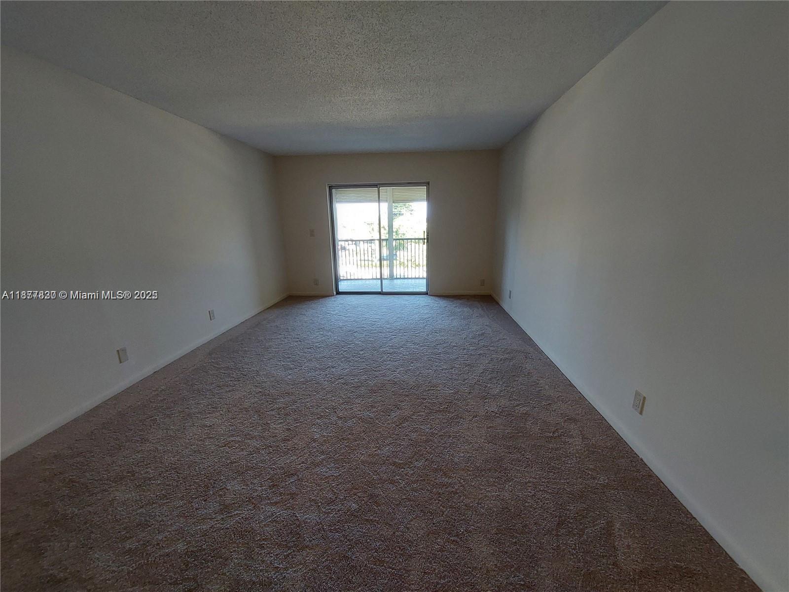 An empty room features beige wall-to-wall carpeting, plain white walls, and a sliding glass door — 257 S Cypress Rd # 438, Pompano Beach FL 33060, POMPANO BEACH, FL