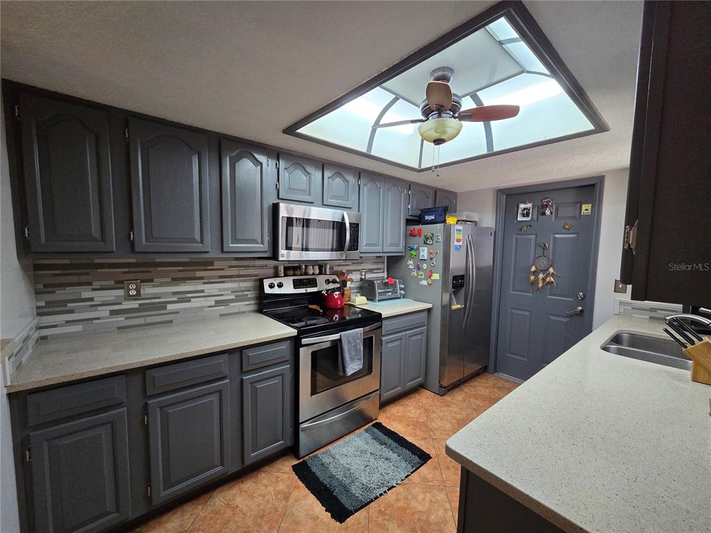 A kitchen features gray cabinets, stainless steel appliances, a tiled backsplash, and a ceiling skylight — 2259 BRANCHWOOD DRIVE, NEW SMYRNA BEACH, FL