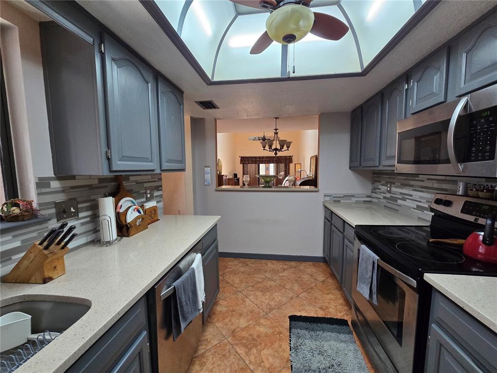 A galley kitchen features gray cabinets, light countertops, a tiled backsplash, and a skylight — 2259 BRANCHWOOD DRIVE, NEW SMYRNA BEACH, FL