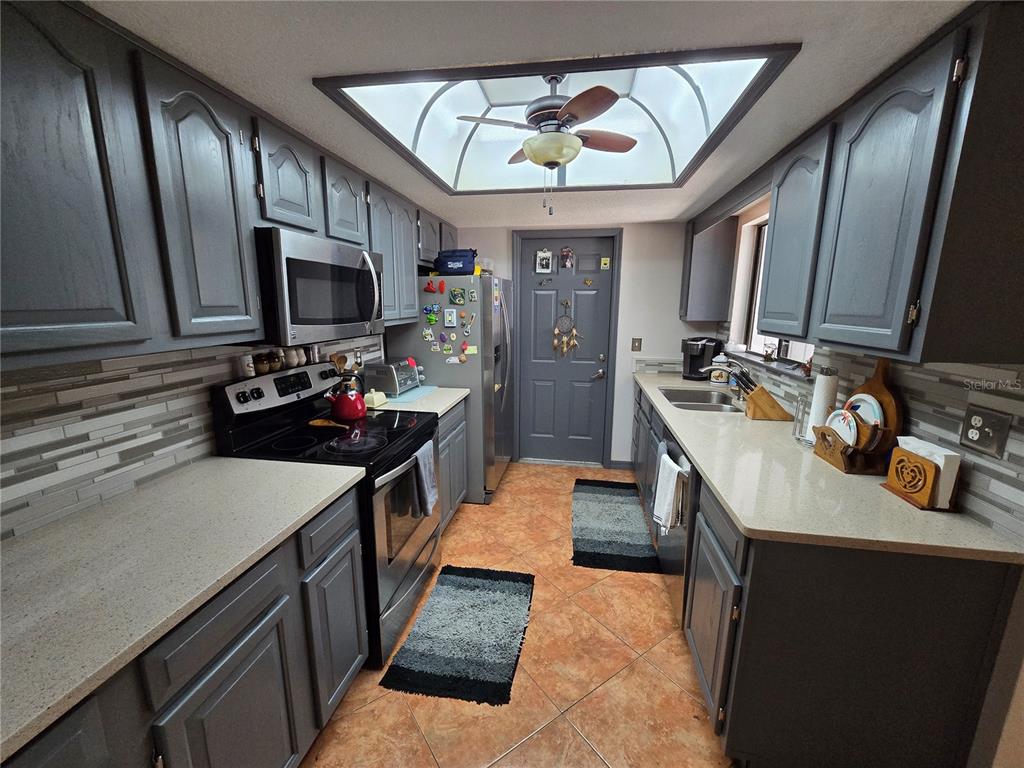 A galley kitchen features gray cabinets, light countertops, a tiled backsplash, and a ceiling skylight — 2259 BRANCHWOOD DRIVE, NEW SMYRNA BEACH, FL