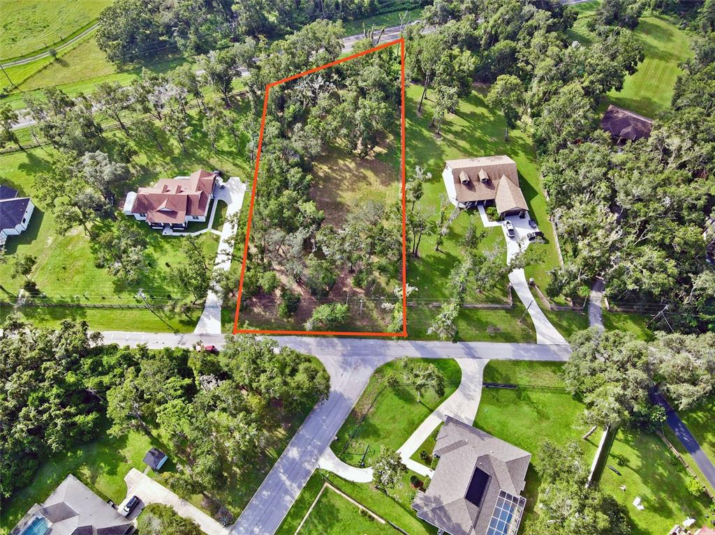 An aerial view shows a vacant, tree-covered lot outlined in orange between two residential houses — 35174 ROTH LANE, DADE CITY, FL