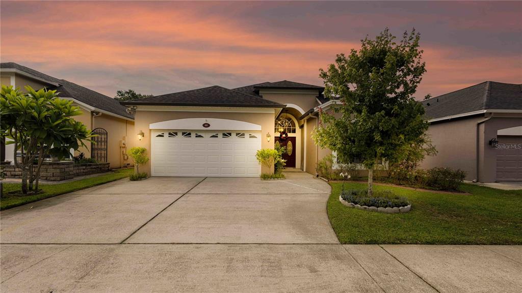 A single-story suburban house with a two-car garage and a concrete driveway at sunset — 935 EKANA GREEN COURT, OVIEDO, FL