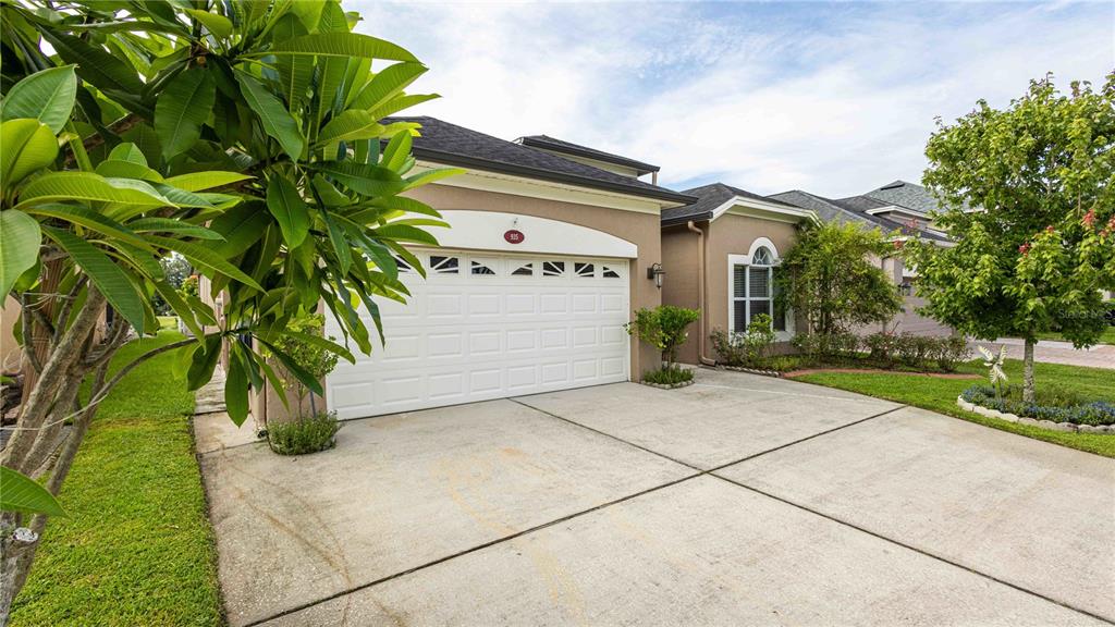 A tan house with a white two-car garage and a concrete driveway under a blue sky — 935 EKANA GREEN COURT, OVIEDO, FL