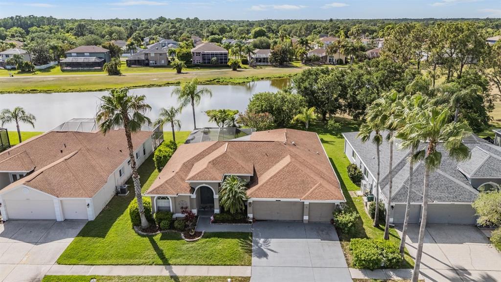An aerial view shows a suburban house with a brown roof, driveway, and palm trees — 15922 MUIRFIELD DRIVE, ODESSA, FL