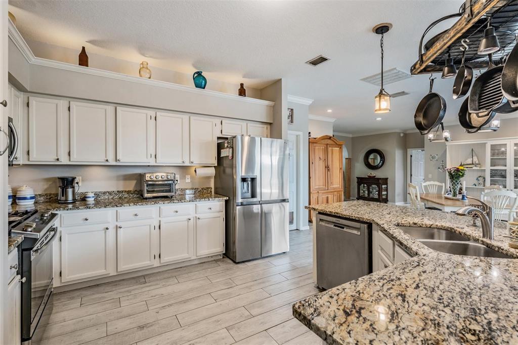 A kitchen features white cabinets, granite countertops, stainless steel appliances, and light wood-look tile flooring — 15922 MUIRFIELD DRIVE, ODESSA, FL