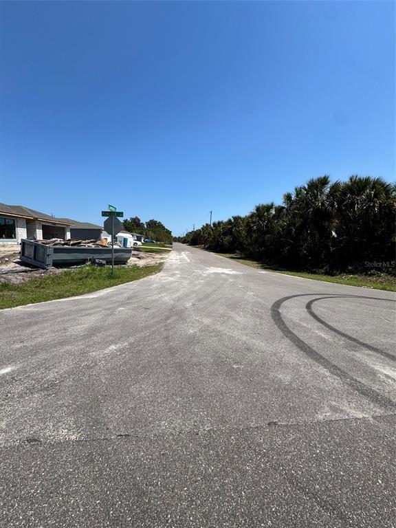 An asphalt road leads past a construction dumpster and a street sign toward palm trees — 598 LAMBRIGHT STREET SW, PALM BAY, FL
