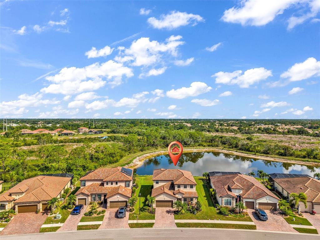 An aerial view shows a row of suburban houses facing a pond under a cloudy sky — 13682 VANCANZA DRIVE, VENICE, FL