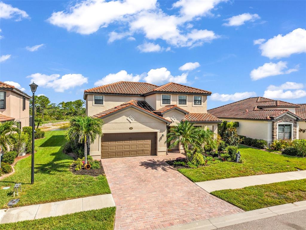 A two-story suburban house with a tan stucco exterior, tile roof, and brick paver driveway — 13682 VANCANZA DRIVE, VENICE, FL