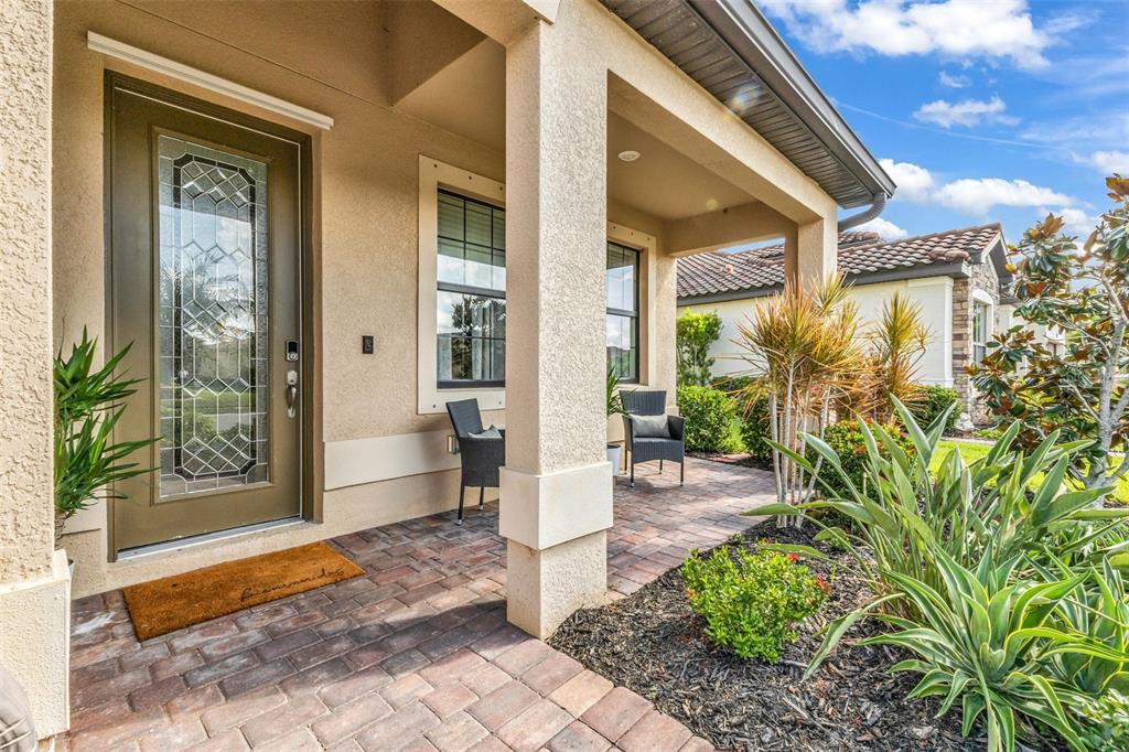 A covered front porch features brick pavers, a glass-paneled door, and a small seating area — 13682 VANCANZA DRIVE, VENICE, FL