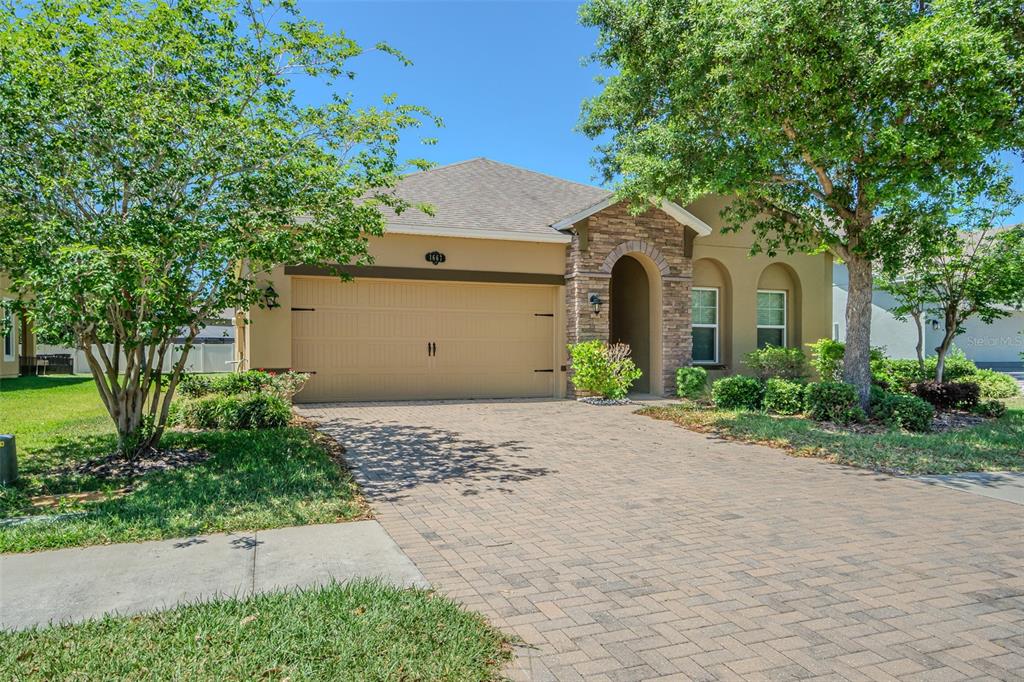 A single-story house with a tan stucco exterior, stone accents, and a paved driveway — 1667 NATURE VIEW DRIVE, LUTZ, FL