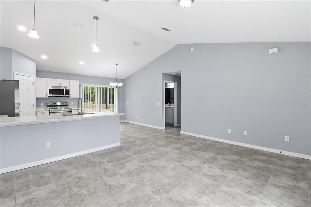 A kitchen with white cabinets and stainless steel appliances overlooks a tiled living area — 3266 SW ADMIRAL LANDING DRIVE, DUNNELLON, FL