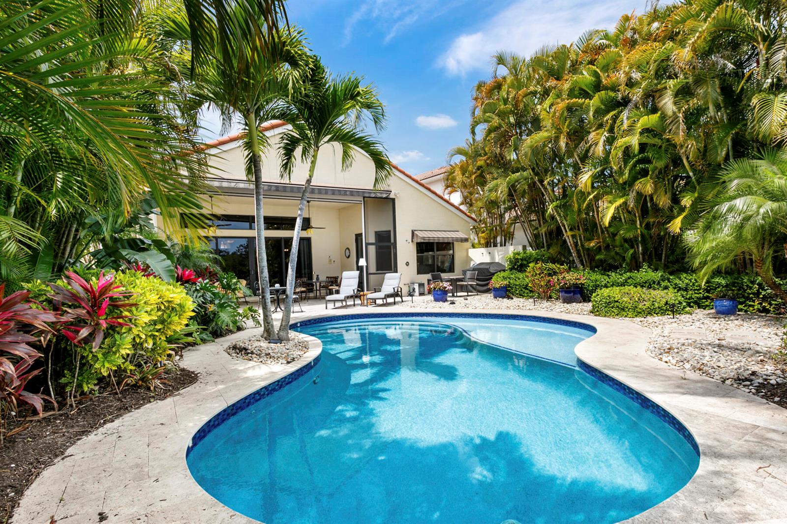 A backyard swimming pool with a patio and lush tropical landscaping behind a residential house — 6700 Fox Hollow Drive, West Palm Beach FL 33412, WEST PALM BEACH, FL