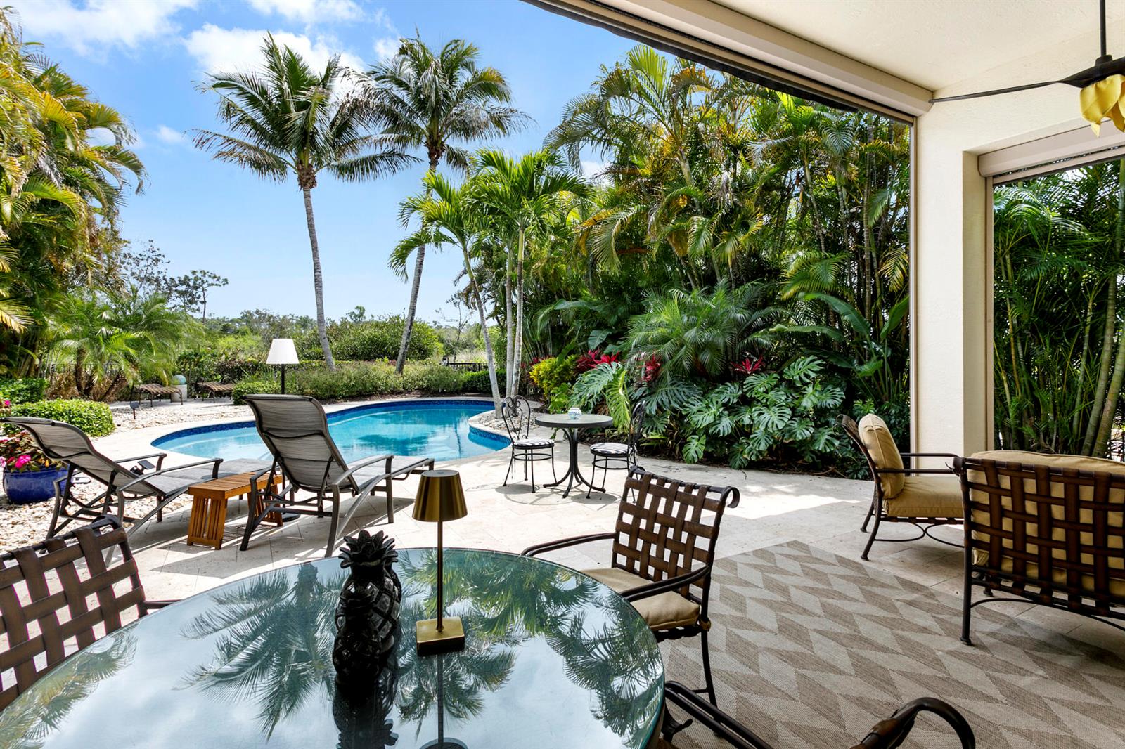 A patio with outdoor furniture and a dining table overlooks a swimming pool and palm trees — 6700 Fox Hollow Drive, West Palm Beach FL 33412, WEST PALM BEACH, FL