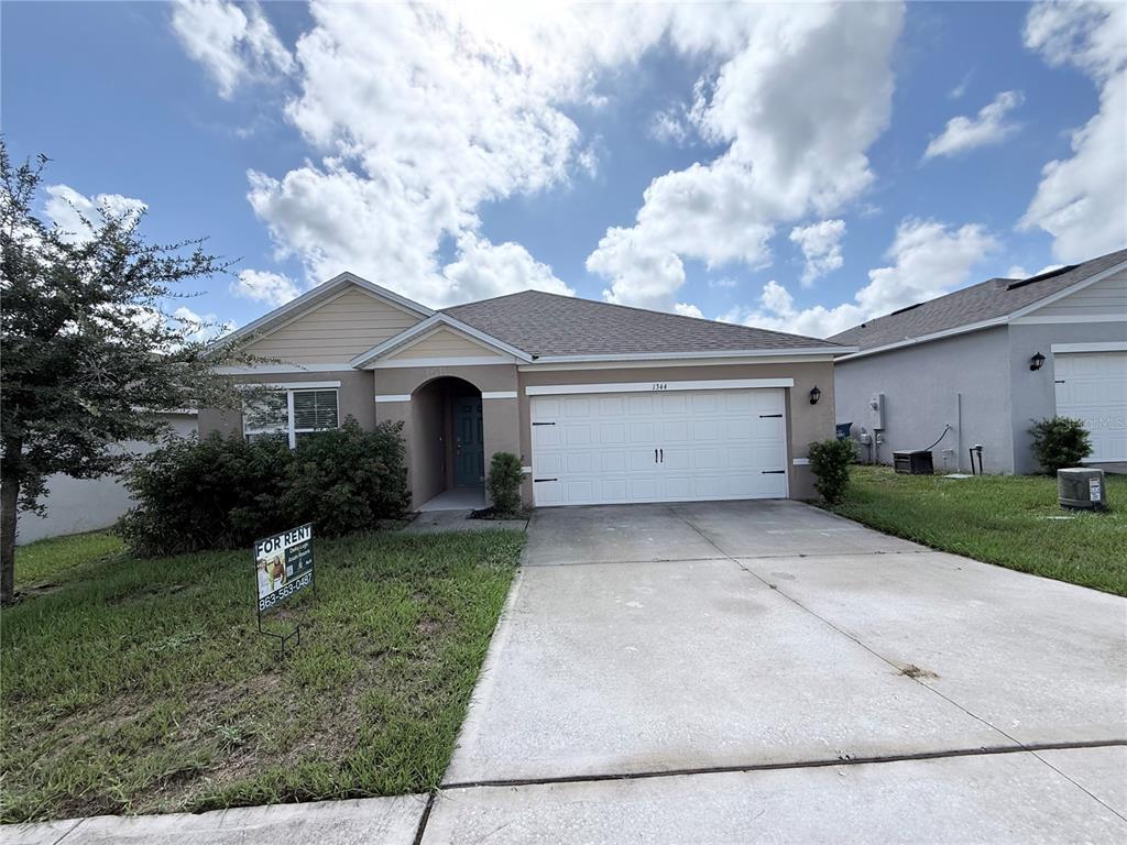 A single-story house with a beige exterior, a two-car garage, and a front lawn — 1344 SUGARWOOD STREET, DAVENPORT, FL