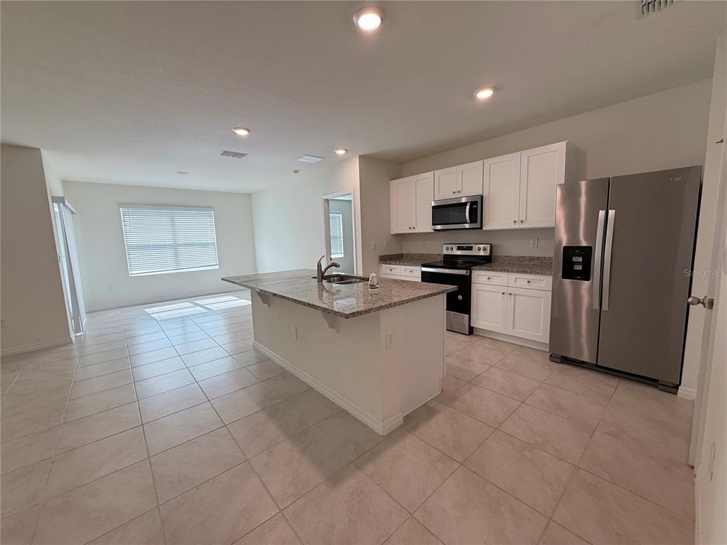 A kitchen with white cabinets, granite countertops, a center island, and stainless steel appliances — 1344 SUGARWOOD STREET, DAVENPORT, FL