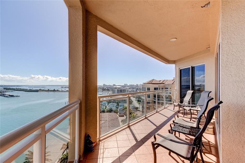 A balcony with tiled flooring and metal chairs overlooks a bay and city skyline — 521 MANDALAY AVENUE UNIT 1109, CLEARWATER BEACH, FL