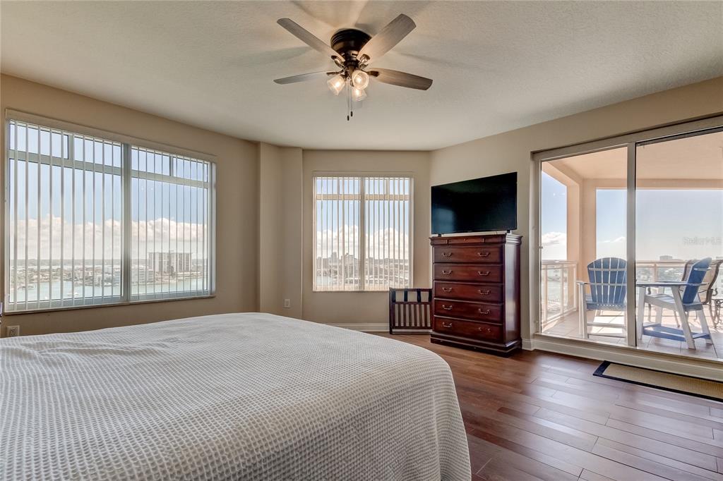 A bedroom features a ceiling fan, wood flooring, a television on a dresser, and balcony access — 521 MANDALAY AVENUE UNIT 1109, CLEARWATER BEACH, FL