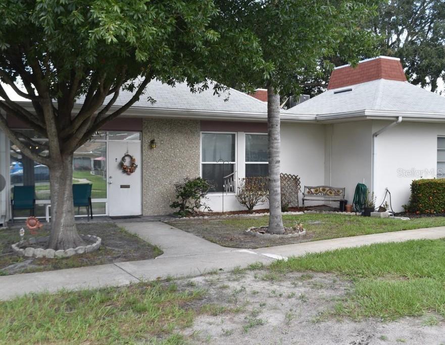 A single-story house with a white door, textured stone siding, and a red-topped roof structure — 4365 TAHITIAN GARDENS CIRCLE UNIT C, HOLIDAY, FL