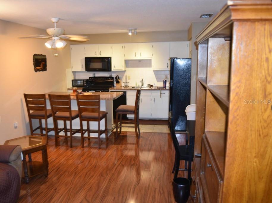 A kitchen with white cabinets, dark appliances, and a breakfast bar with four wooden chairs — 4365 TAHITIAN GARDENS CIRCLE UNIT C, HOLIDAY, FL
