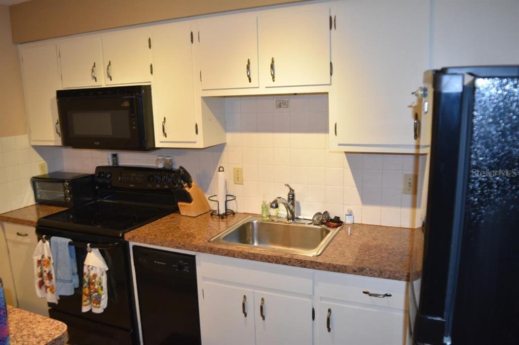 A kitchen features white cabinets, a black stove, a stainless steel sink, and granite countertops — 4365 TAHITIAN GARDENS CIRCLE UNIT C, HOLIDAY, FL