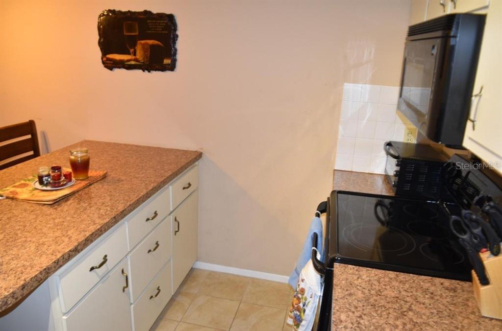 A kitchen features light cabinets, granite-look countertops, a black stove, and a wall-mounted picture — 4365 TAHITIAN GARDENS CIRCLE UNIT C, HOLIDAY, FL