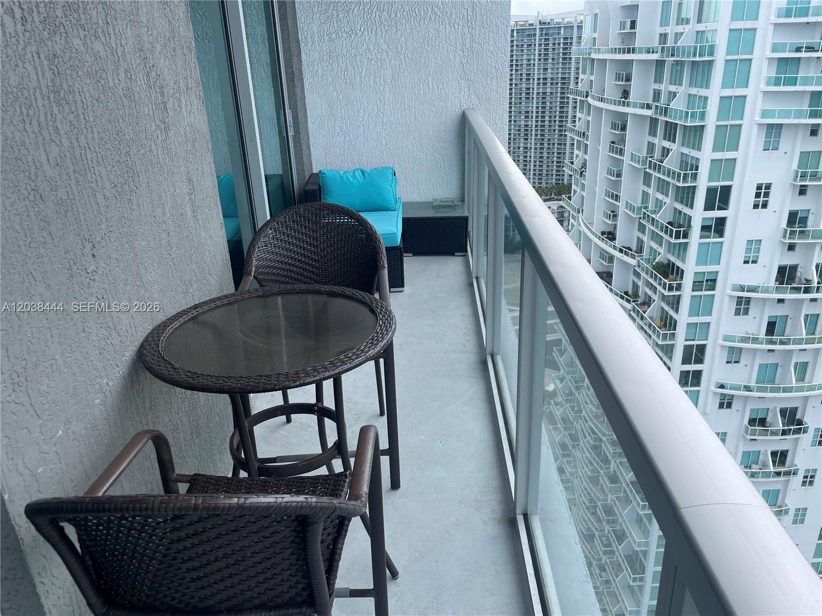 A balcony features a small round table, two chairs, and a cushioned bench overlooking buildings — 55 SE 6th St, Miami FL 33131, MIAMI, FL