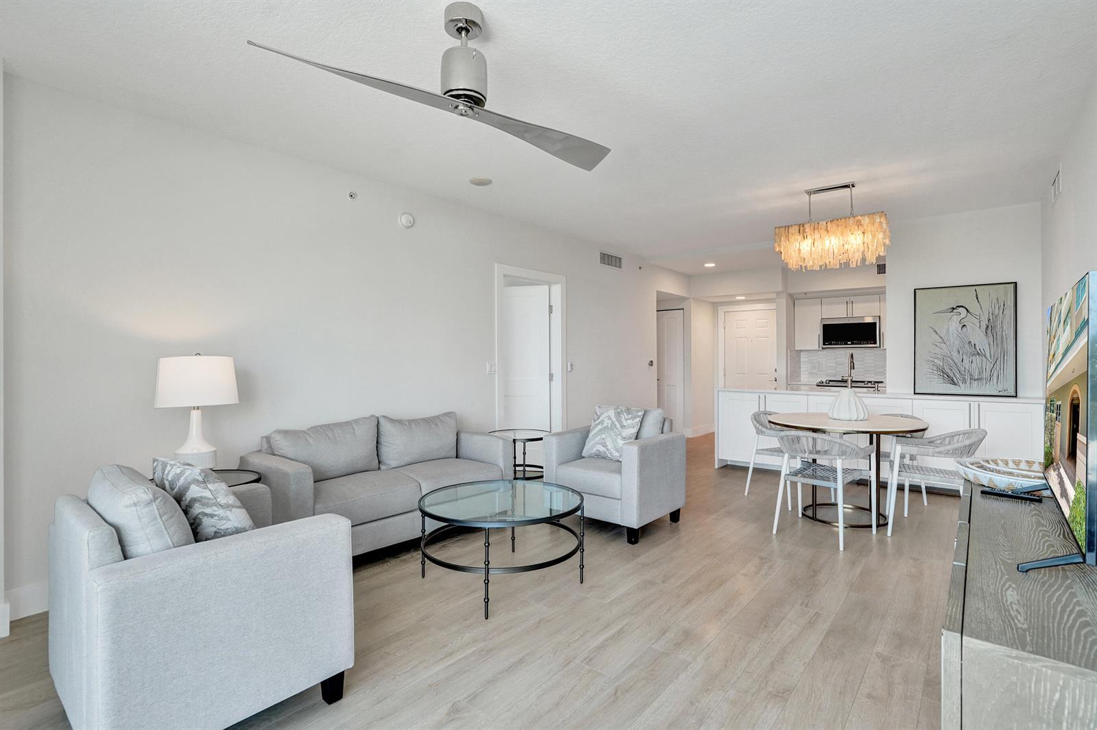 A living room and dining area with light wood floors, gray furniture, and a ceiling fan — 700 E Boynton Beach Boulevard # 406, Boynton Beach FL 33435, BOYNTON BEACH, FL