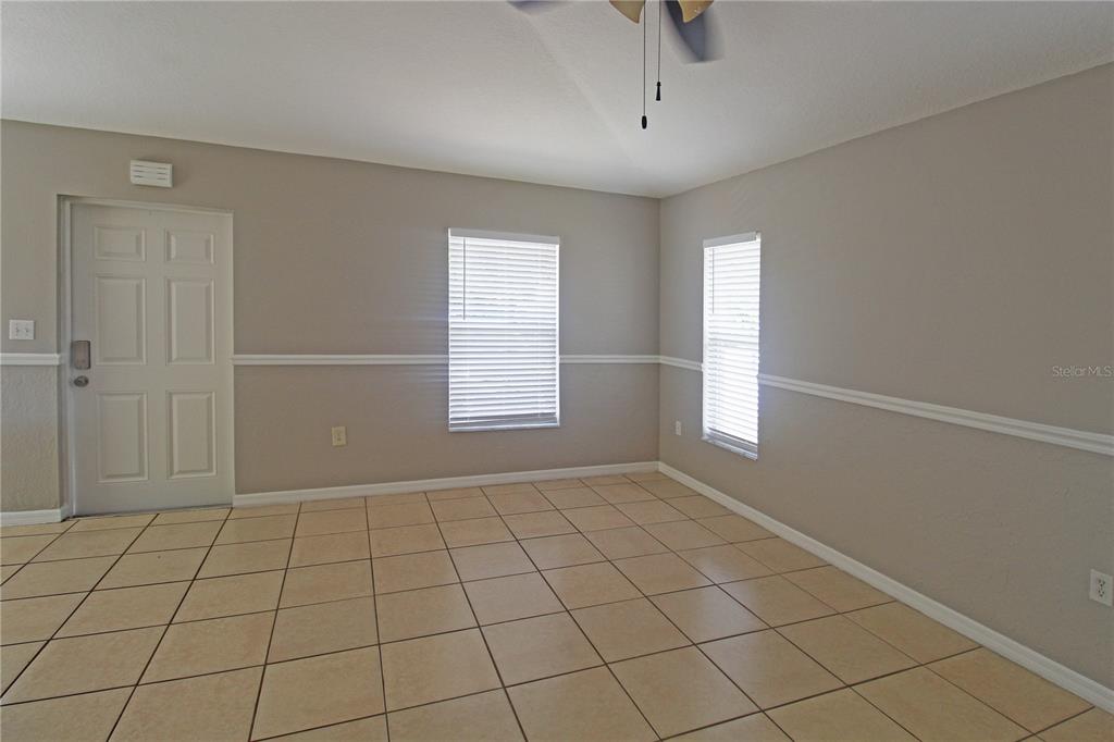 An empty room features beige walls, a white door, two windows with blinds, and tiled flooring — 5445 ALTOONA STREET, SARASOTA, FL