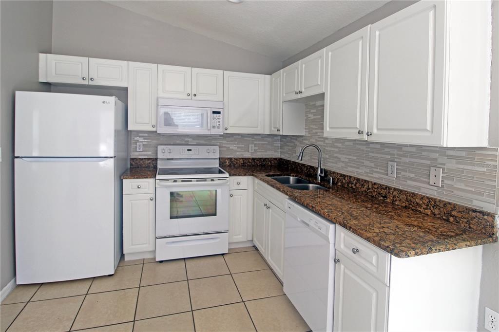 A kitchen with white cabinets, granite countertops, tile flooring, and white appliances — 5445 ALTOONA STREET, SARASOTA, FL