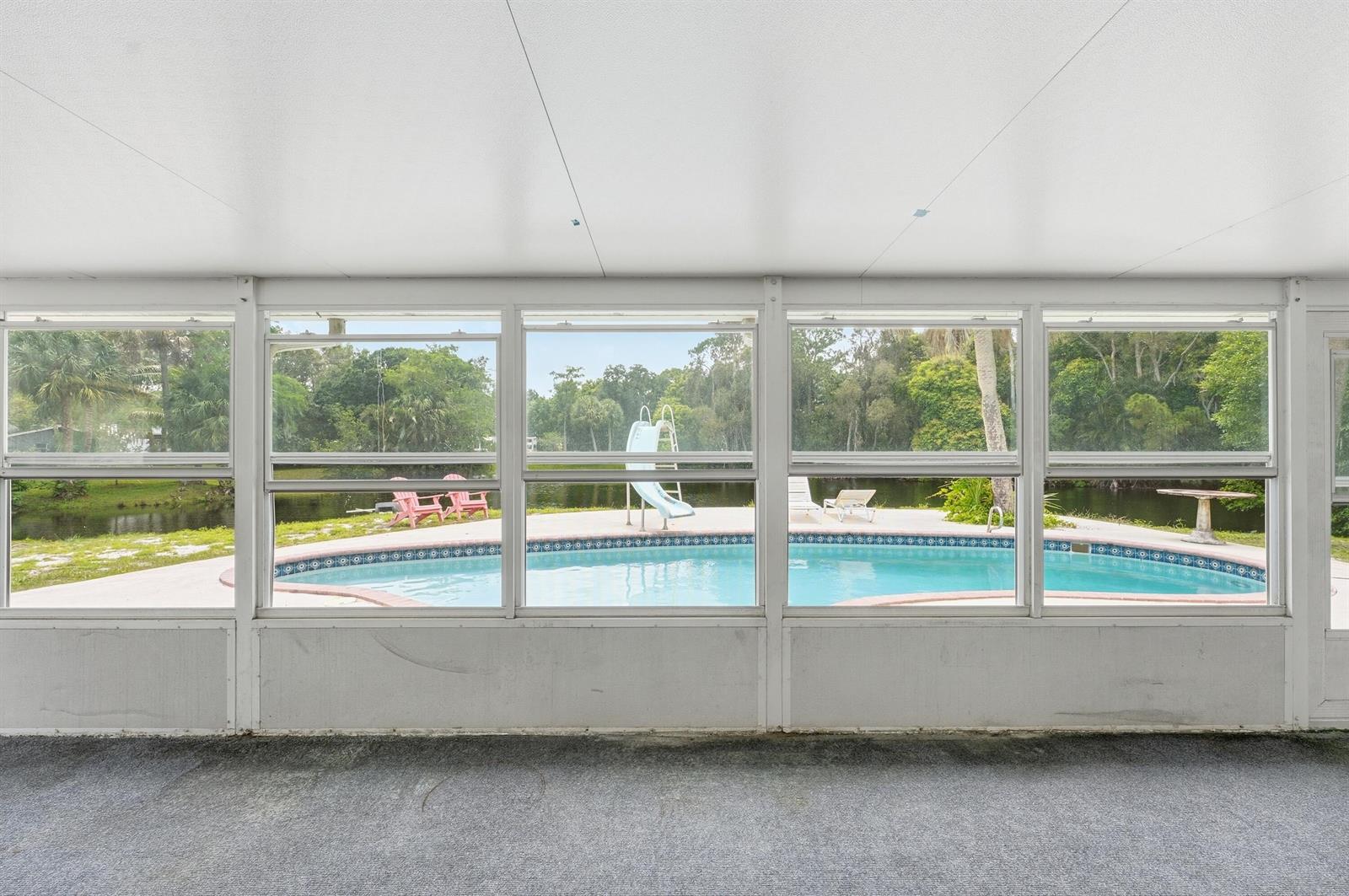 A carpeted sunroom with large windows overlooks a backyard swimming pool and a pond — 7689 Lawrence Road, Boynton Beach FL 33436, BOYNTON BEACH, FL