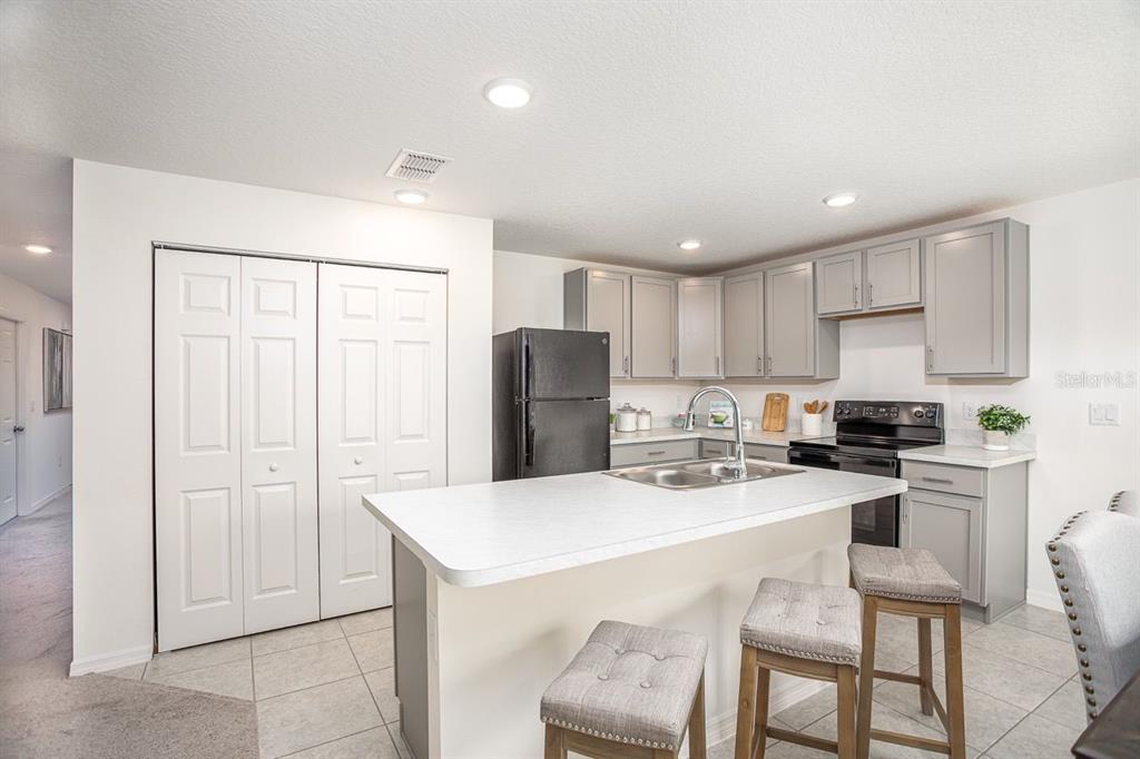 A kitchen features gray cabinets, a white island with bar stools, and black appliances — 426 OHIO LANE, POINCIANA, FL