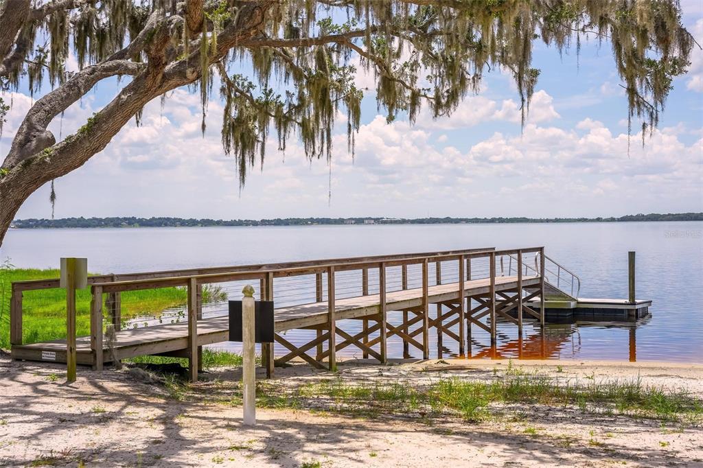 A wooden pier extends into a calm lake beneath a large, moss-draped oak tree — 1025 GREEN RIDGE COURT, MINNEOLA, FL