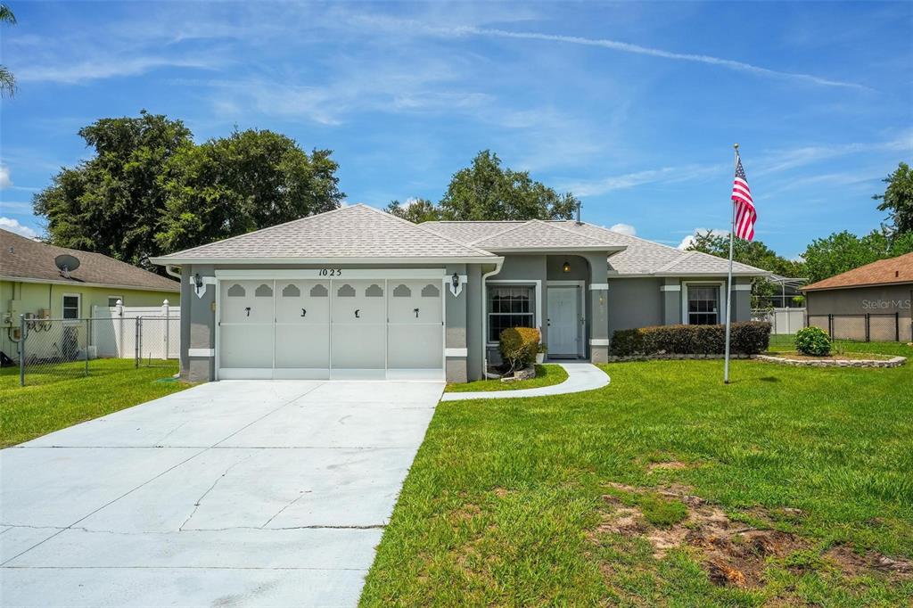 A single-story gray house with a white garage door, a front lawn, and an American flag — 1025 GREEN RIDGE COURT, MINNEOLA, FL