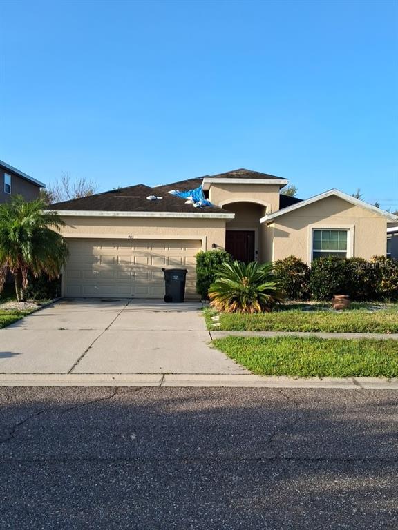 A single-story suburban house with a tan stucco exterior, a two-car garage, and a blue tarp — 405 BLAKELY COURT, RUSKIN, FL