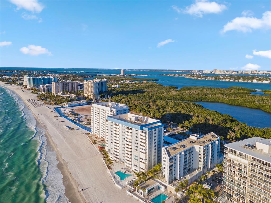 An aerial view shows several beachfront high-rise condominiums along a sandy coastline near a bay — 1750 BENJAMIN FRANKLIN DRIVE UNIT 1D, SARASOTA, FL