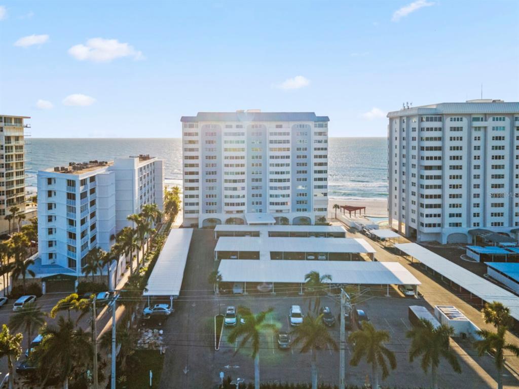 An aerial view shows three beachfront apartment buildings with covered parking lots in the foreground — 1750 BENJAMIN FRANKLIN DRIVE UNIT 1D, SARASOTA, FL