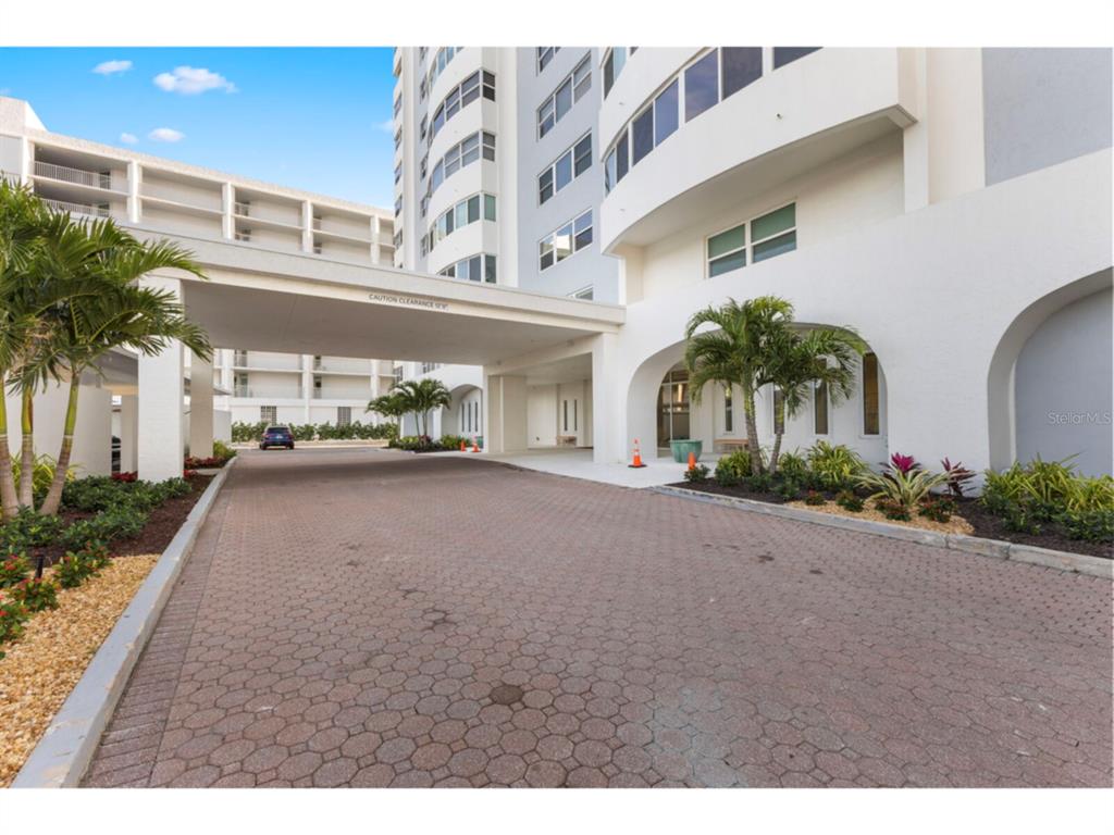 A paved driveway leads to the covered entrance of a multi-story white residential building — 1750 BENJAMIN FRANKLIN DRIVE UNIT 1D, SARASOTA, FL