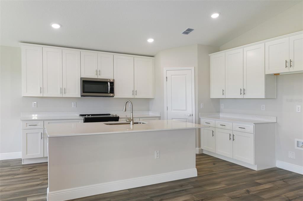 A kitchen features white cabinets, quartz countertops, a central island, and wood-look flooring — 6103 SW 97TH STREET, OCALA, FL