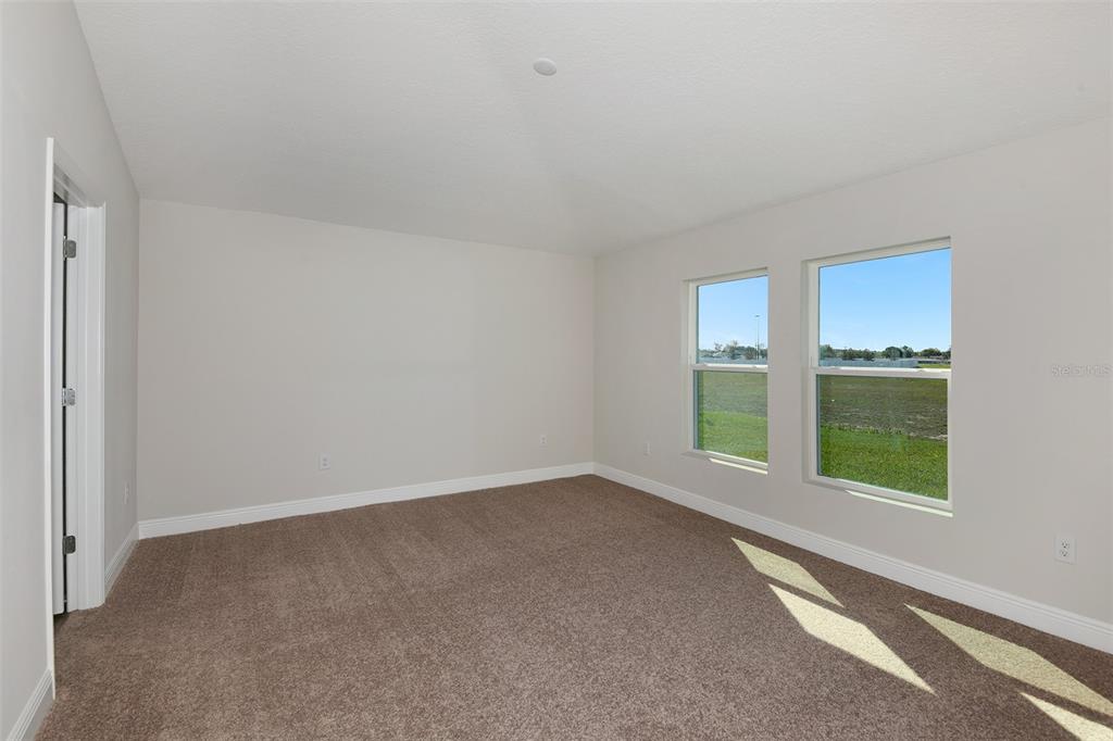 An empty bedroom features beige carpet, light gray walls, and two windows overlooking a field — 6103 SW 97TH STREET, OCALA, FL