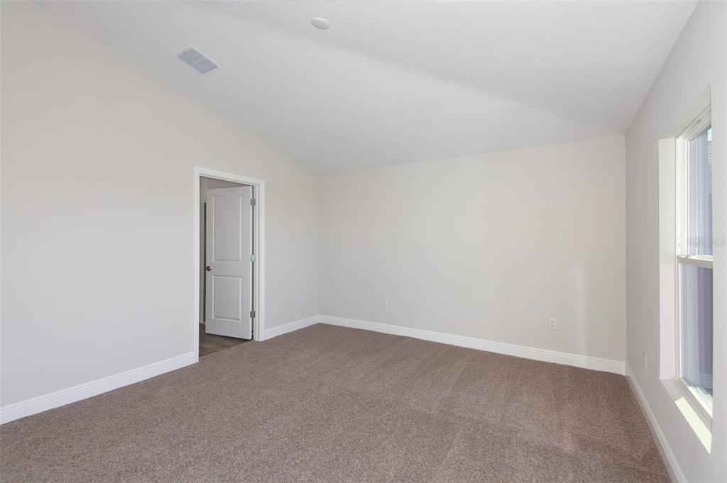 An empty bedroom with beige carpet, light-colored walls, a vaulted ceiling, and a doorway — 6103 SW 97TH STREET, OCALA, FL