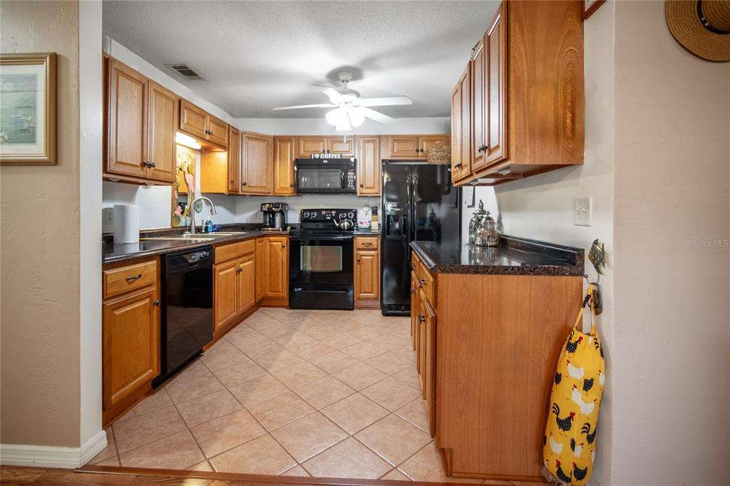 A kitchen features wood cabinets, black appliances, dark countertops, and light-colored tile flooring — 2835 NORDMAN AVENUE, NEW SMYRNA BEACH, FL