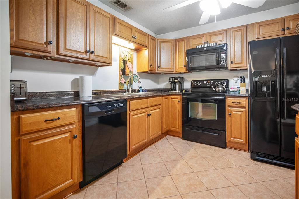 A kitchen with oak cabinets, black appliances, dark countertops, and light-colored tile flooring — 2835 NORDMAN AVENUE, NEW SMYRNA BEACH, FL