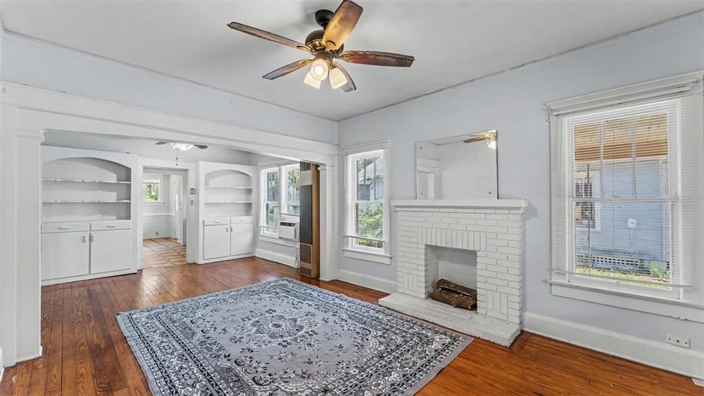 A living room with hardwood floors, a white brick fireplace, and built-in shelving units — 506 S MCKAY AVENUE, LAKELAND, FL