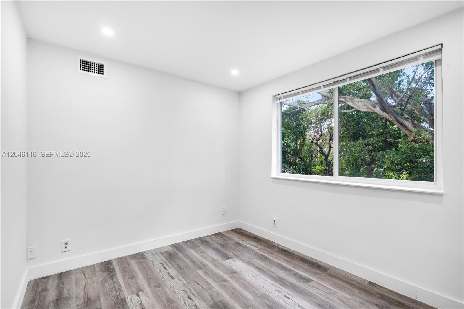 An empty room features white walls, wood-look flooring, recessed lighting, and a large window — 6445 NW 2nd Ave # 19, Miami FL 33150, MIAMI, FL