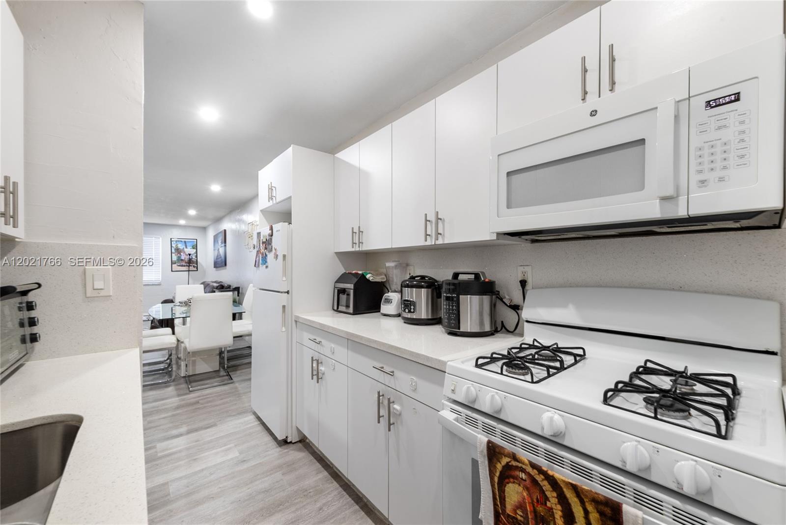 A white kitchen features modern cabinetry, a gas stove, and light wood-look flooring — HIALEAH, FL