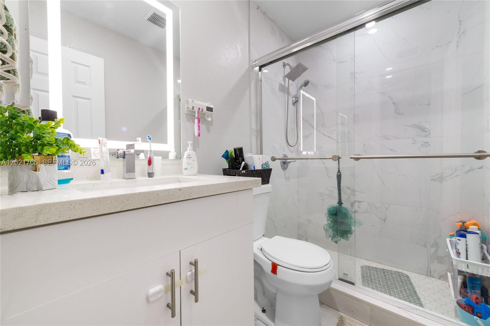 A bathroom features a white vanity, a toilet, and a glass-enclosed walk-in shower — HIALEAH, FL