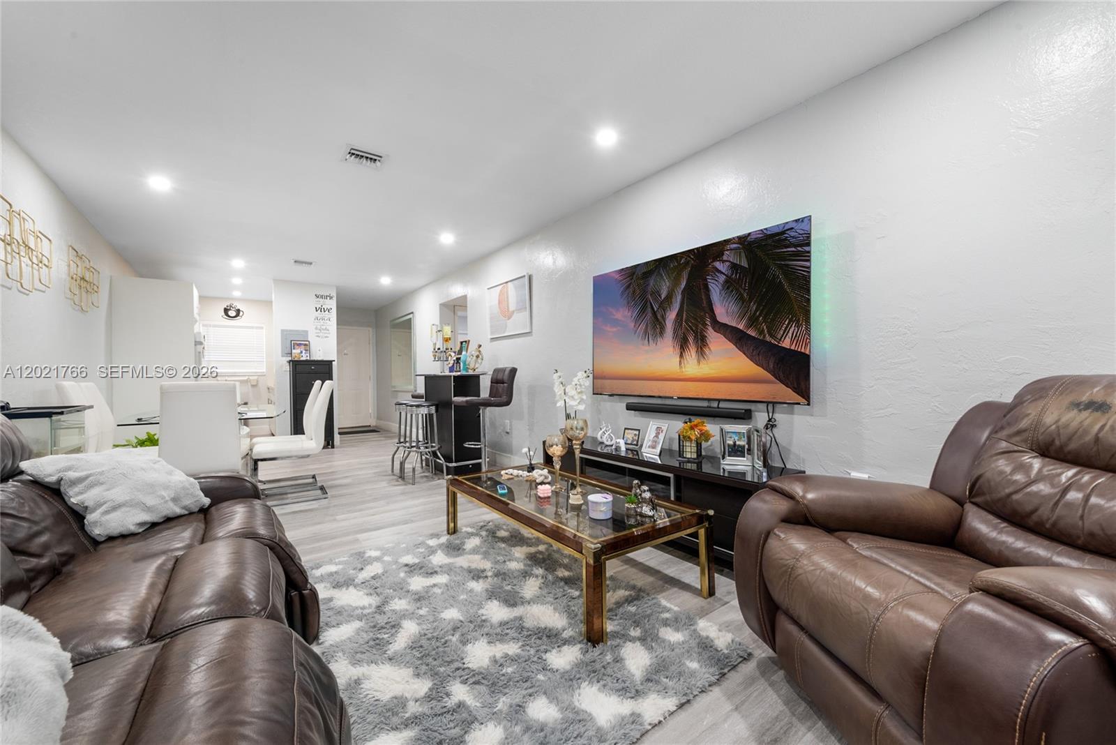 A living room features brown leather sofas, a glass coffee table, and a wall-mounted television — HIALEAH, FL